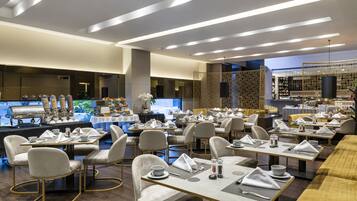 A modern restaurant with multiple dining tables and chairs, a buffet area, and a kitchen in the background.