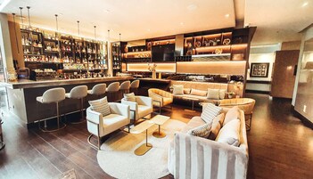 A modern bar area with multiple seating options, a well-stocked liquor shelf, and a cozy seating area with sofas and chairs.