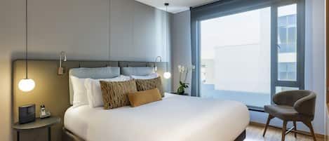 Et moderne hotelværelse med en stor seng, sengeborde, en stol og et stort vindue med udsigt.