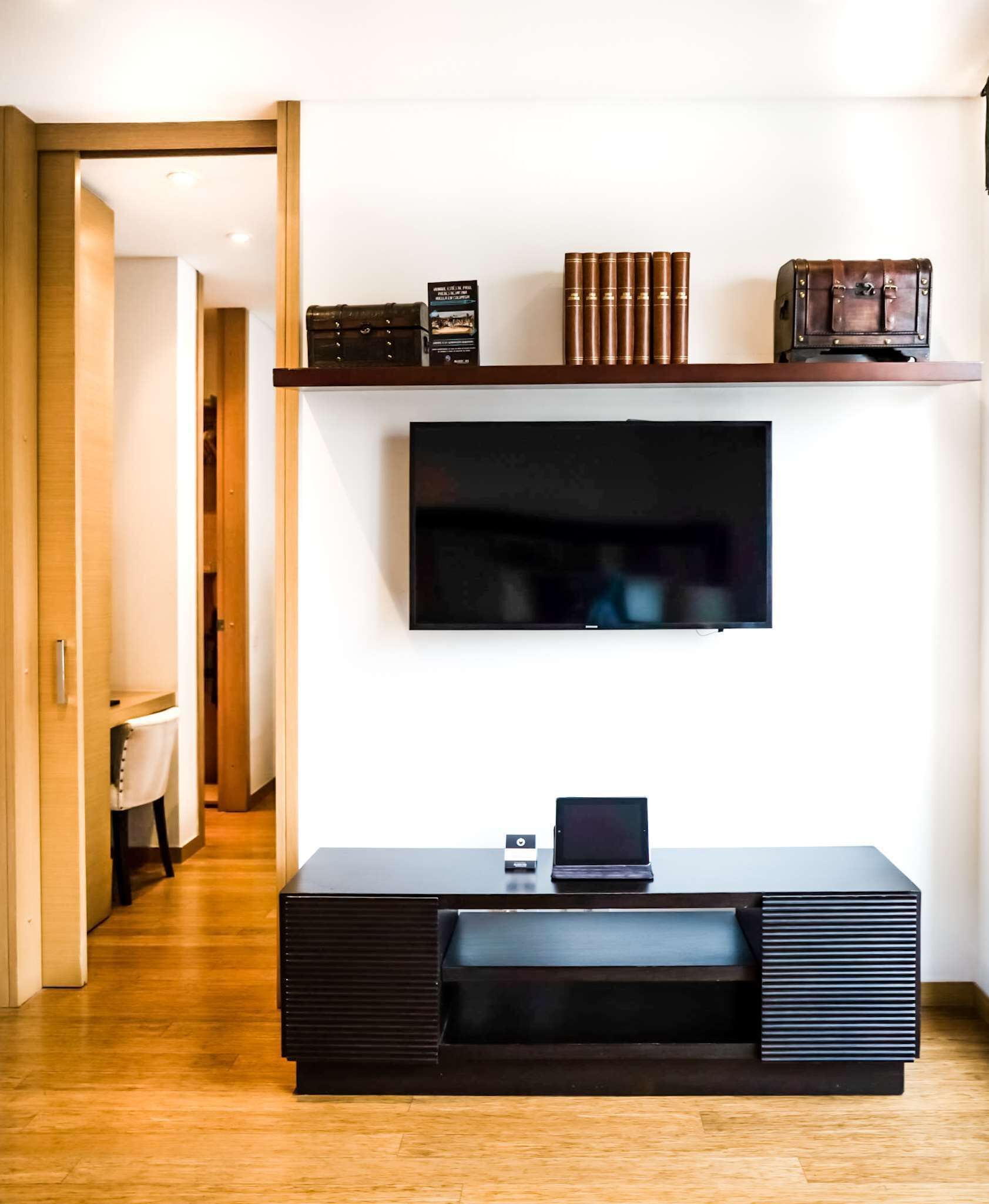 A modern living room with a flat-screen TV mounted on the wall, a dark wooden entertainment unit below, and a laptop on top.