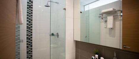 A modern bathroom with a glass-enclosed shower, a large mirror, and a granite countertop with toiletries.