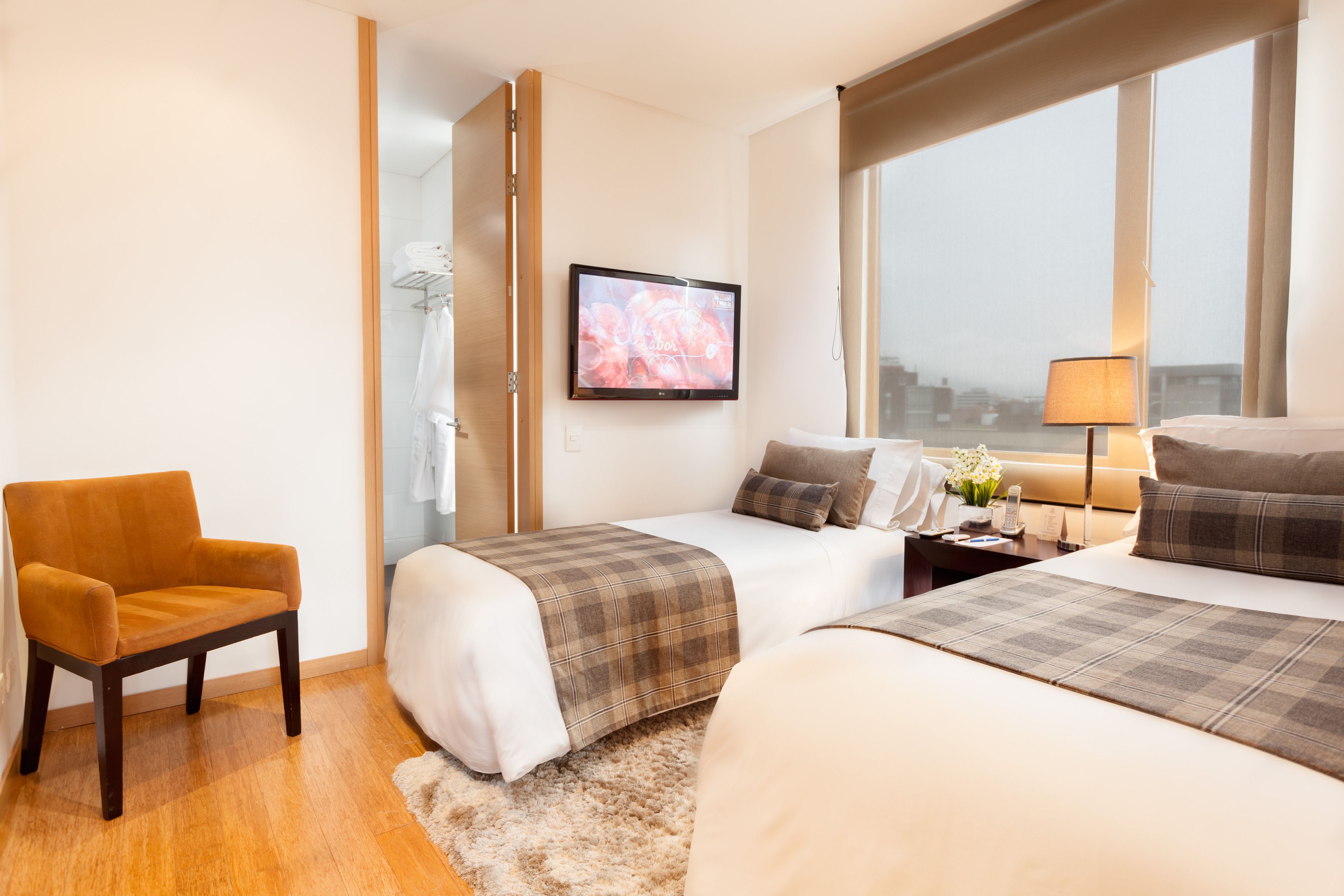 A hotel room with two beds, a chair, a TV, a nightstand, and a window with a view of the city.