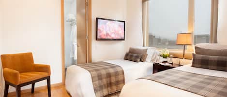 A hotel room with two beds, a chair, a TV, a nightstand, and a window with a view of the city.