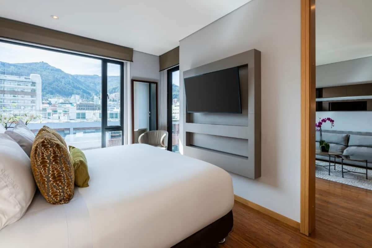 Ein modernes Hotelzimmer mit einem großen Bett, einem flachbildfernseher an der Wand und Blick auf die Stadt durch große Fenster.