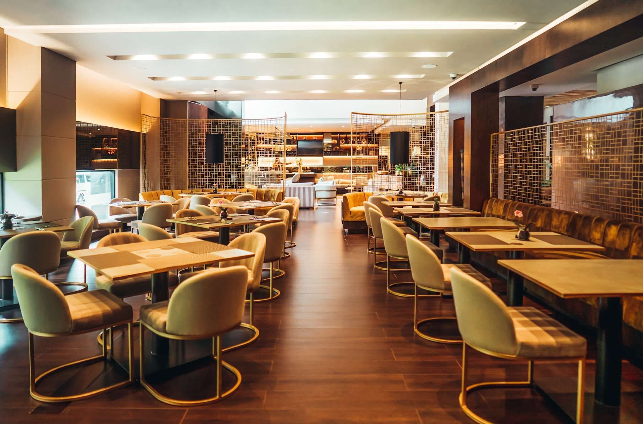 Een ruim restaurant met verschillende eetgedeeltes, waaronder zitjes en tafels, en een centraal gelegen ruimte met een televisie.