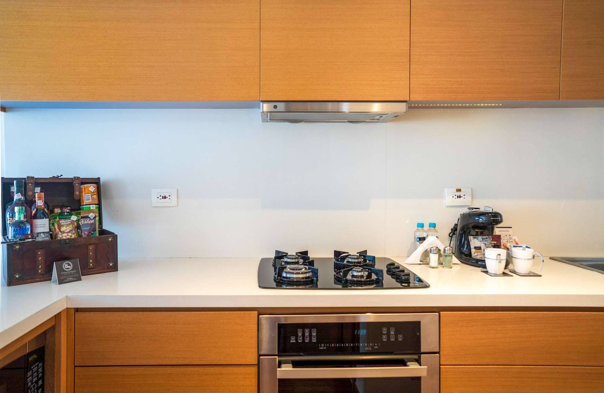Una cocina moderna con armarios de madera, una campana extractora de acero inoxidable, una cafetera y un refrigerador pequeño.
