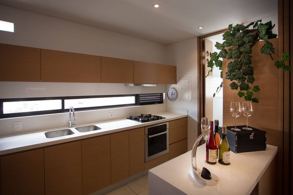 A modern kitchen with wooden cabinets, a stainless steel sink, a gas stove, and a built-in oven. There are wine bottles and glasses on the counter.