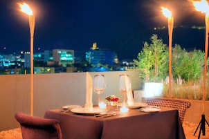 A table set for two with candles, a vase of flowers, and a city view at night.