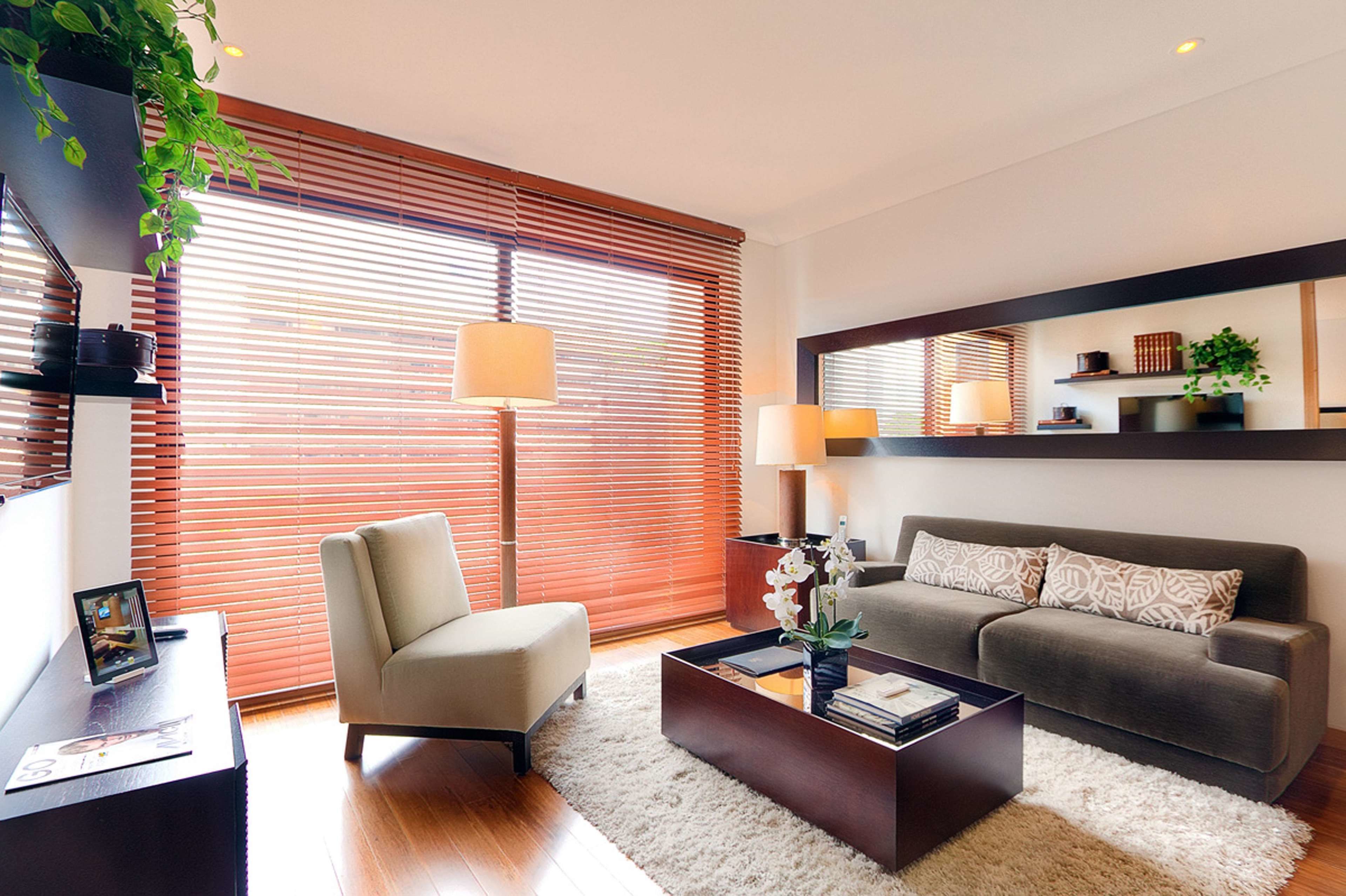 A modern living room with a sofa, armchair, coffee table, and a large window with blinds.