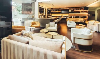 Zona lounge moderna con divani e poltrone, un bar con scaffali pieni di bottiglie e un televisore.