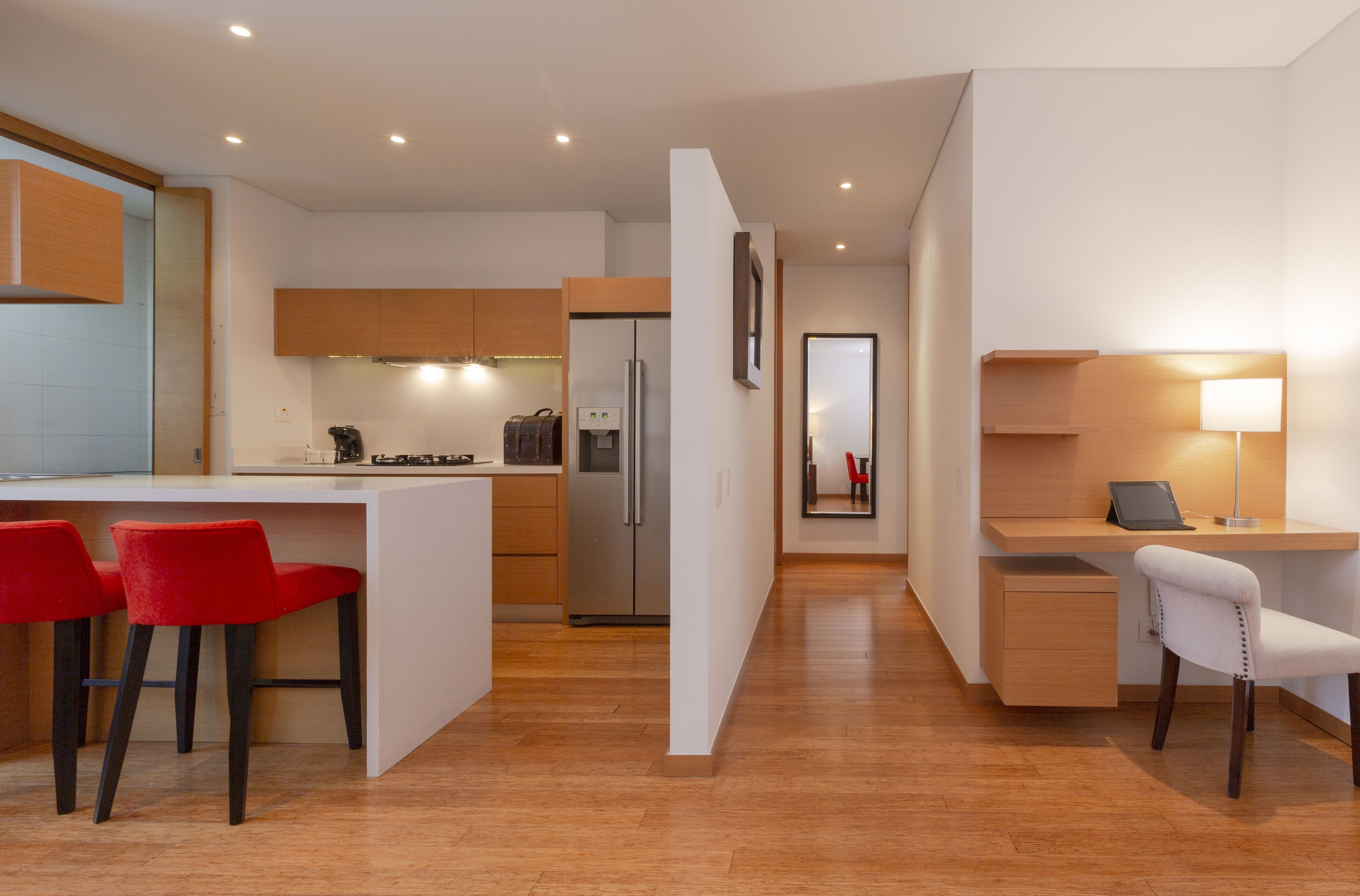 A modern kitchen with a central island, red bar stools, and a built-in refrigerator.