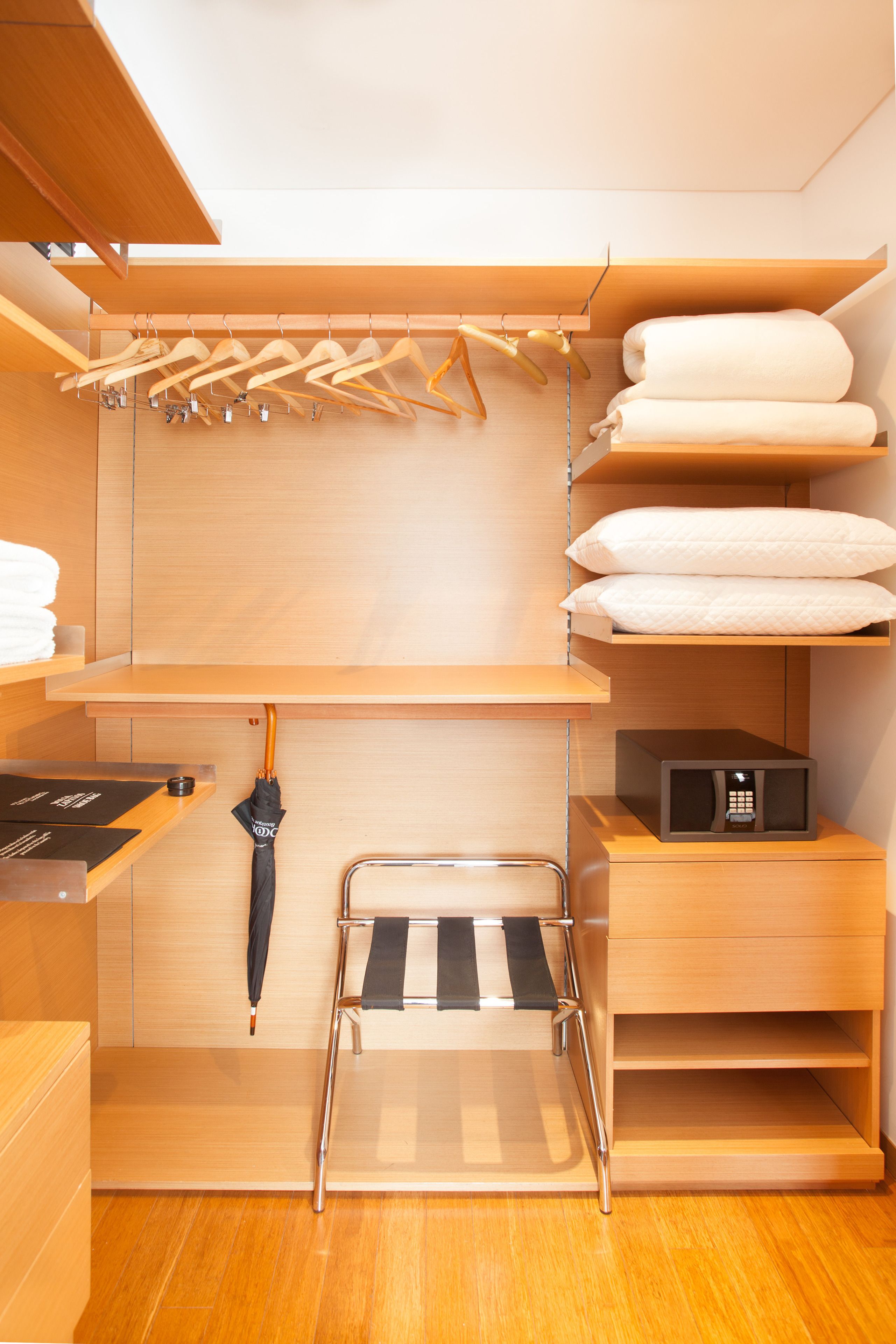 A compact, modern closet with wooden shelves, a hanging rack, and a compact microwave.