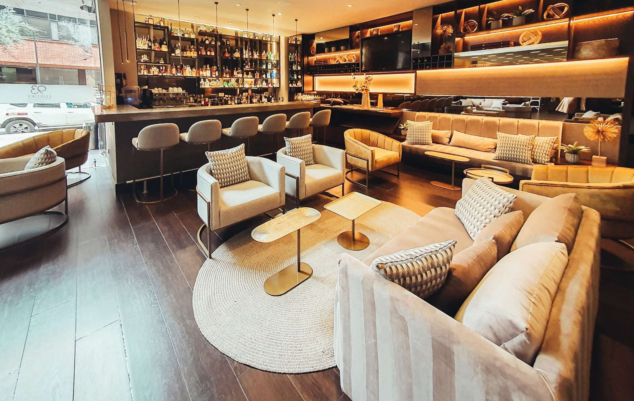A modern bar area with multiple seating options, including sofas and chairs, and a well-stocked liquor shelf.