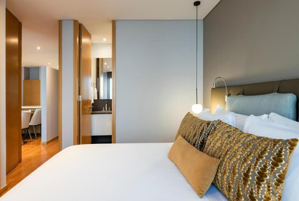 A modern hotel room with a large bed, a desk, and a mirror.