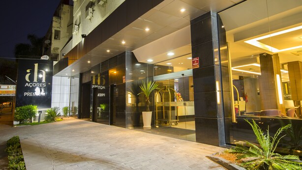 A modern hotel entrance with glass doors, a potted plant, and a sign for "Acores Premium." - Açores Premium (Porto Alegre)