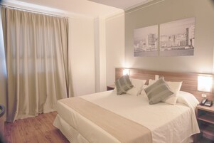 Habitación de hotel con una cama grande, una obra de arte urbana en la pared, cabecero de madera y una mesita de noche con lámpara.