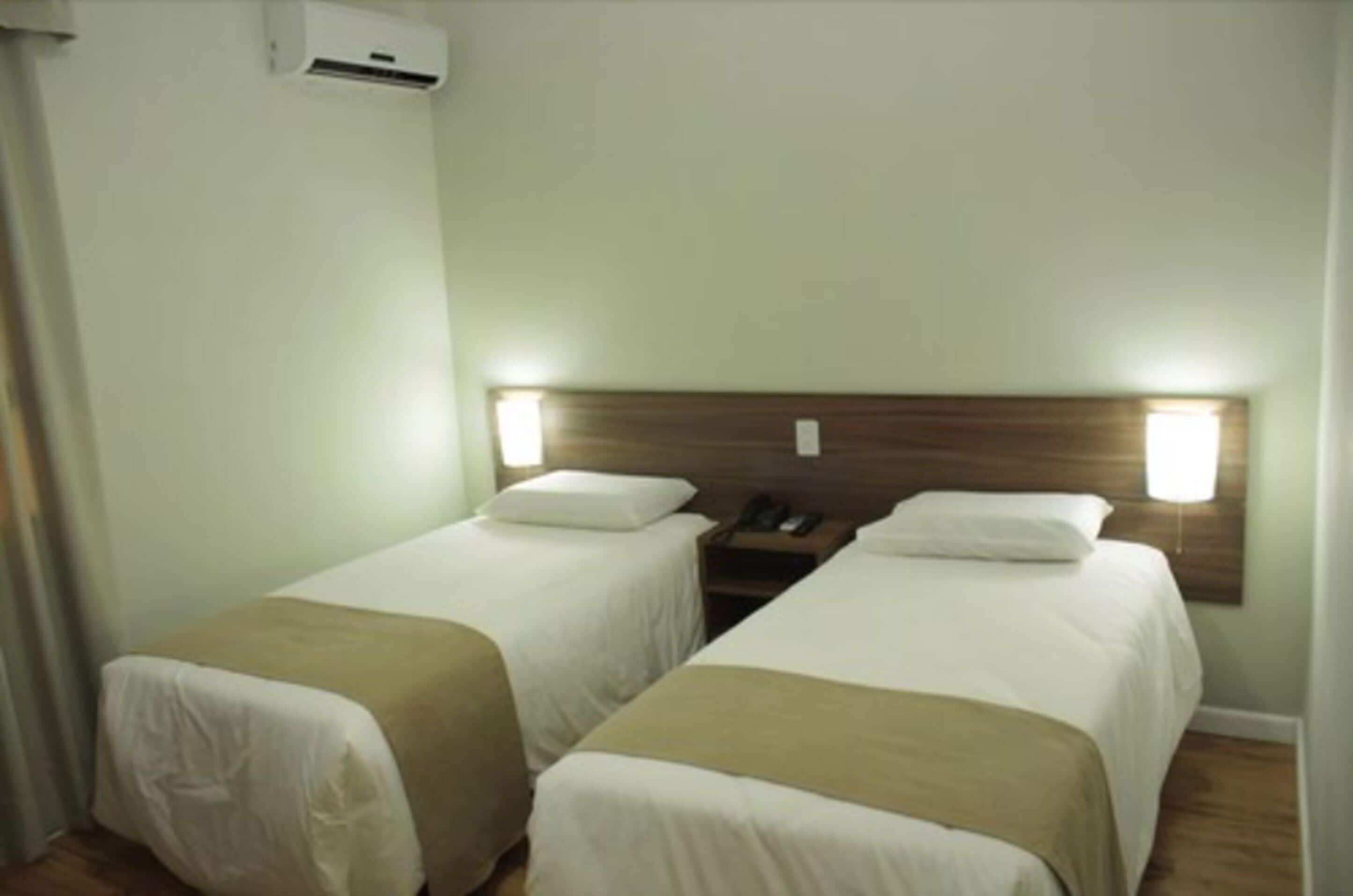 A hotel room with two single beds, a wooden headboard, bedside lamps, and a telephone.