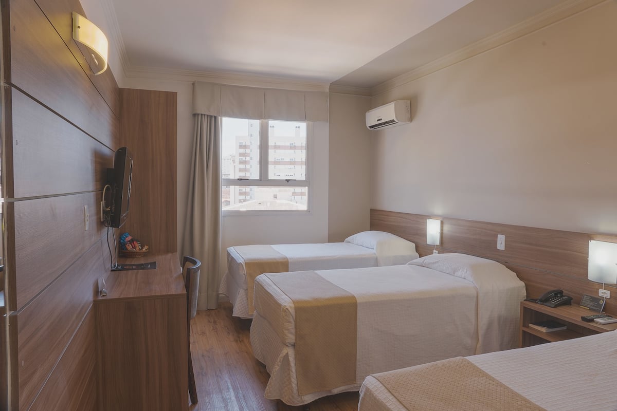 A hotel room with two beds, a wooden desk, a TV, and a window with curtains.