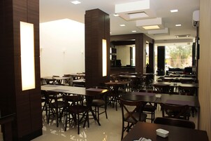 Un restaurante espacioso con varias mesas y sillas, techos altos con iluminación empotrada y vistas al exterior a través de amplias ventanas.