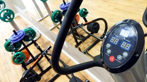 A stationary bike with a digital display, surrounded by weightlifting equipment. - Açores Premium (Porto Alegre)
