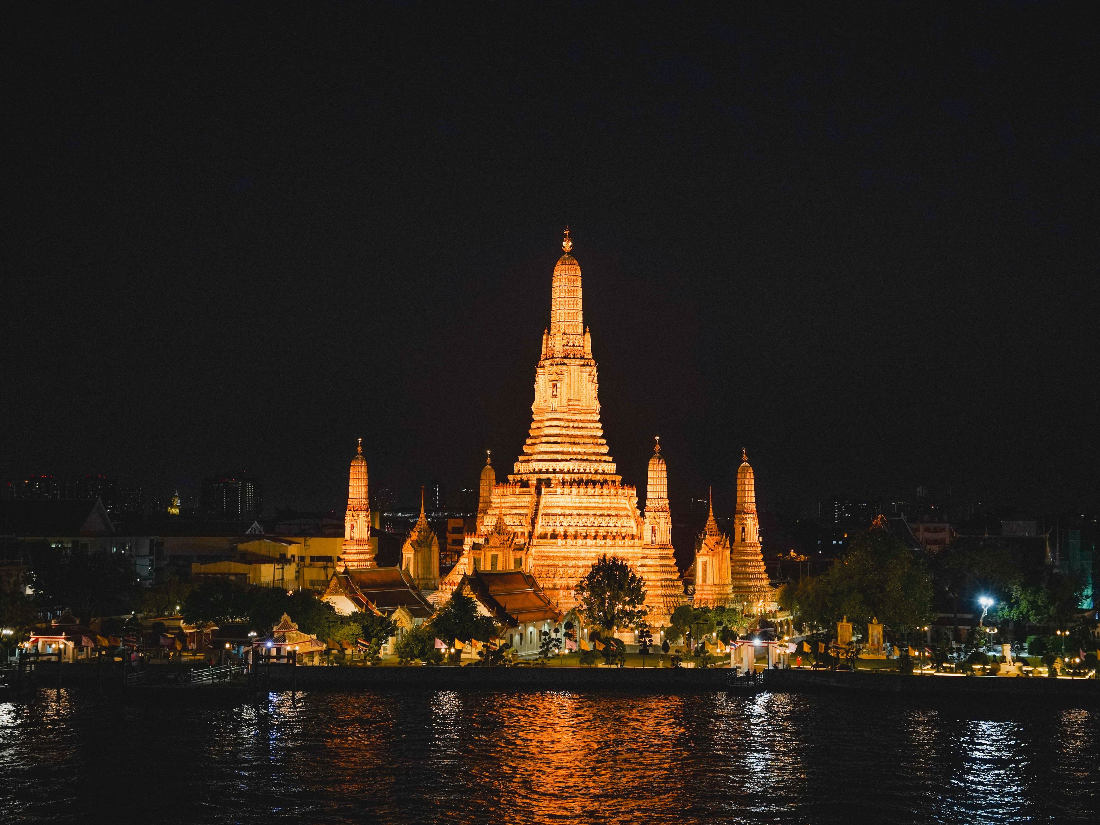 A night view of a temple complex with multiple spires and a reflection on the water.