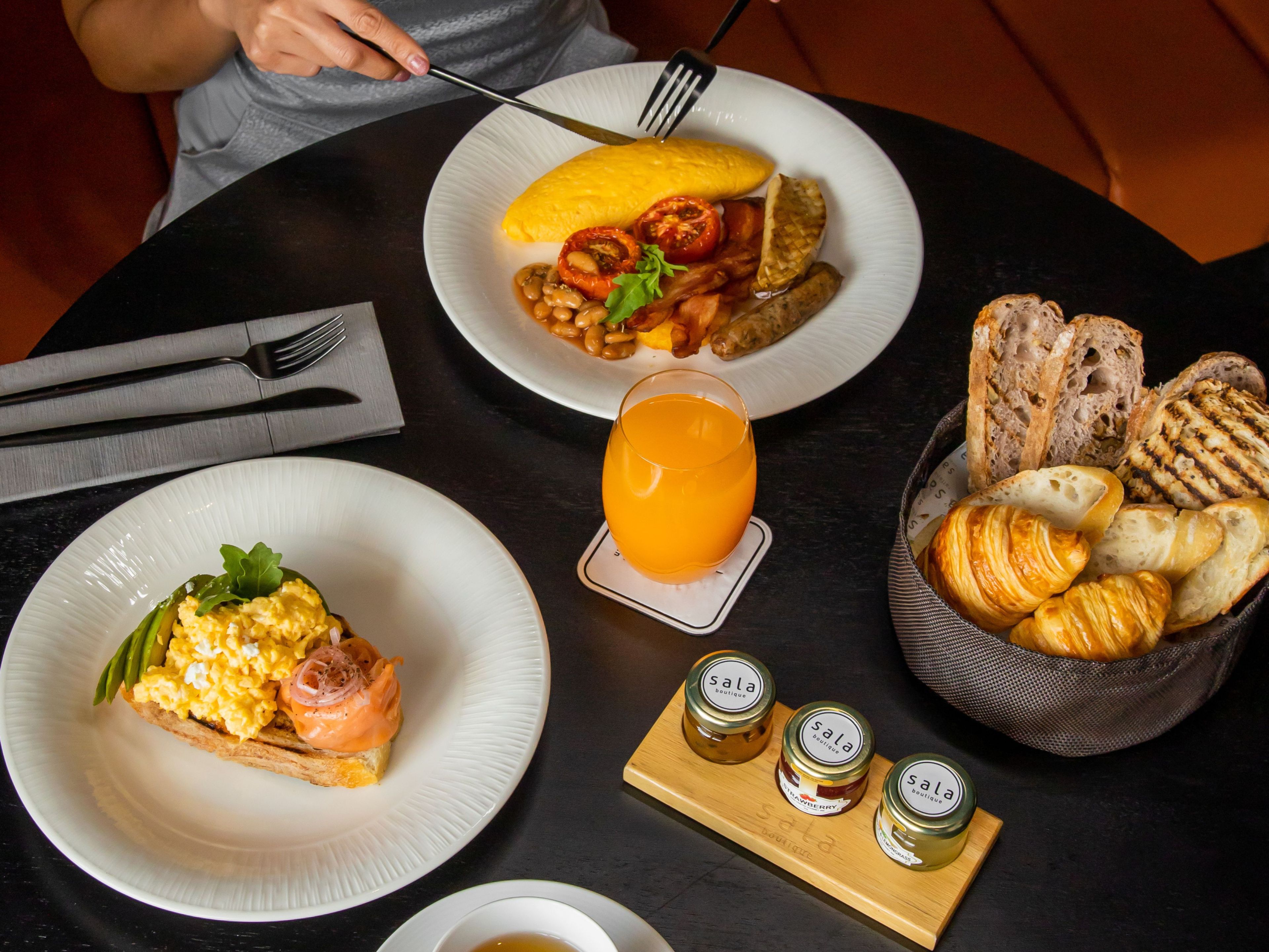 A table set with breakfast items including eggs, toast, and bread, with condiments and a glass of orange juice.
