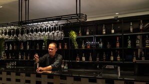 A bar area with a bartender preparing drinks, shelves with liquor bottles, and a hanging glass rack. - Sala Rattanakosin Bangkok (Bangkok)