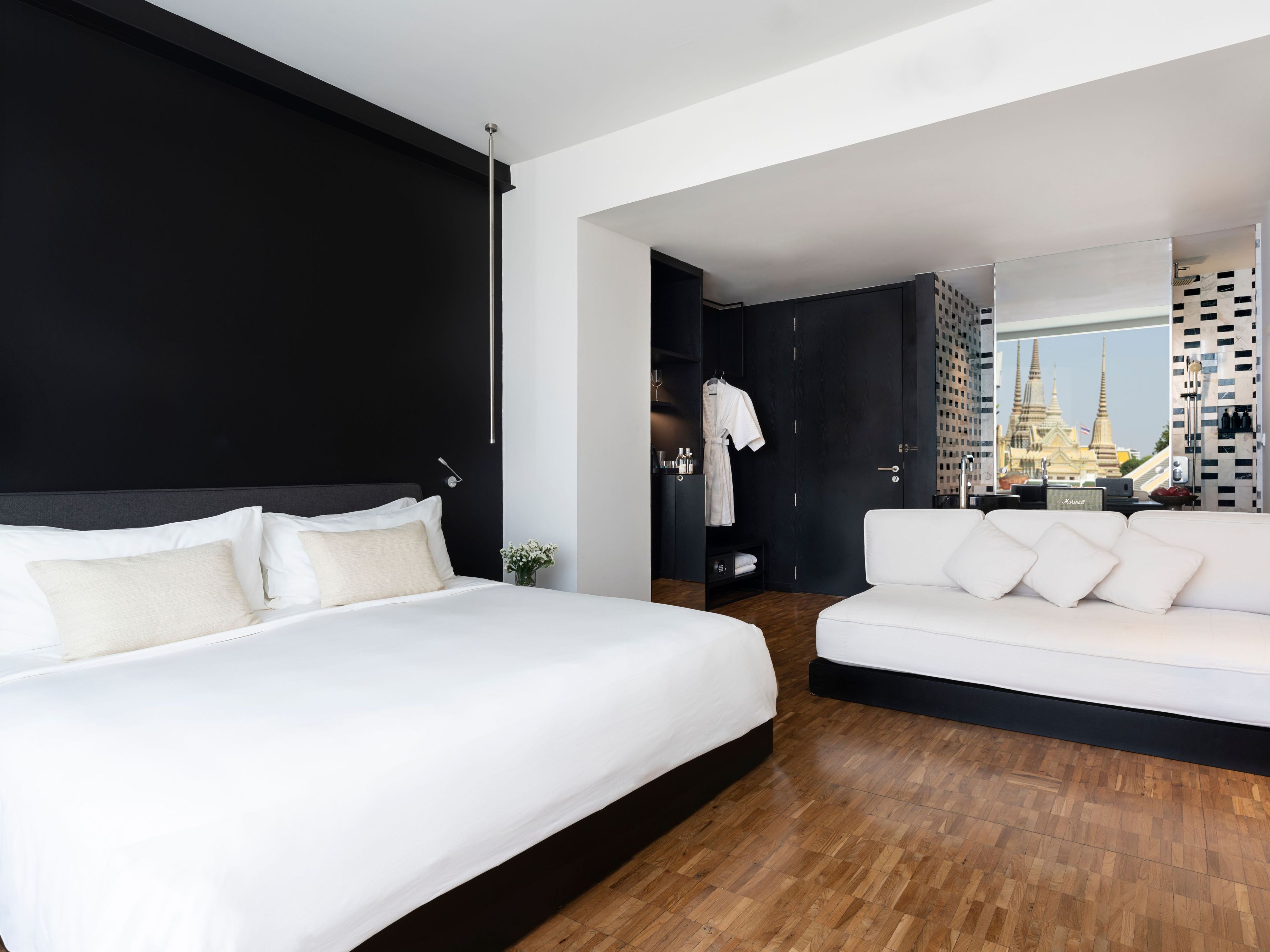 A modern hotel room with a large bed, a white sofa, and a view of a temple through a window.