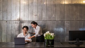 A modern office setting with a wooden wall, a desk with a laptop, a monitor, and a vase with white flowers. - Sala Rattanakosin Bangkok (Bangkok)