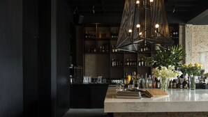Una zona de bar con mostrador de mármol, estanterías con botellas y dos taburetes.