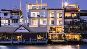 Un hotel de varios pisos con un restaurante en la planta baja, un balcón con asientos y vistas al río.