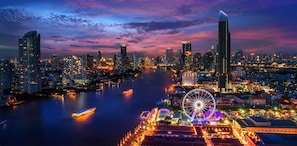 A cityscape at dusk with illuminated buildings, a river, and a Ferris wheel. - Sala Rattanakosin Bangkok (Bangkok)