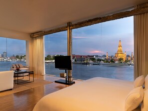 A modern hotel room with a large bed, a TV, and a view of a cityscape and river. - Sala Rattanakosin Bangkok (Bangkok)