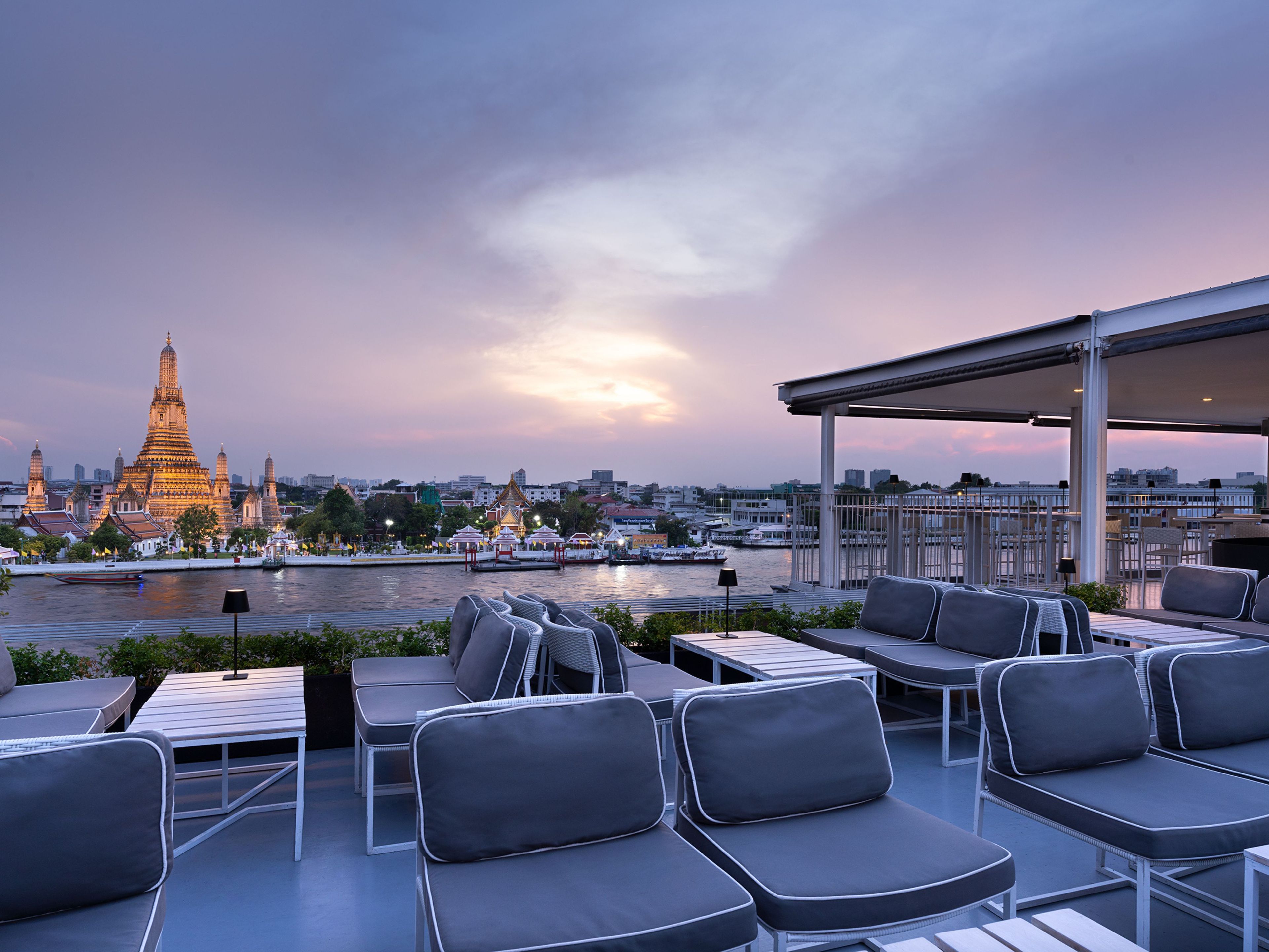 A rooftop terrace with outdoor seating and a view of a cityscape and a temple.