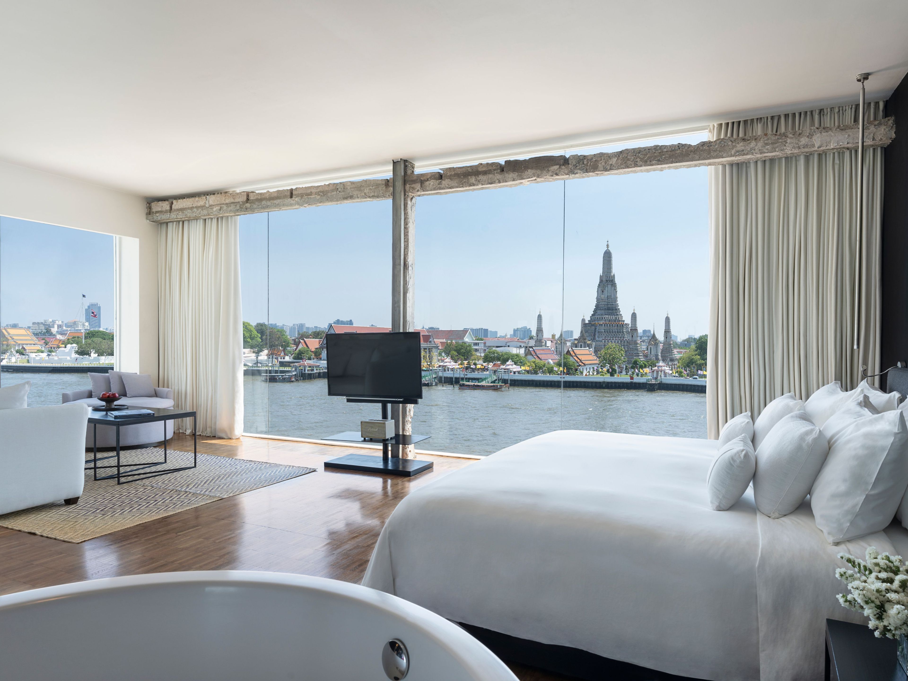 A hotel room with a large bed, a sitting area with a table, a TV, and a view of a cityscape and water.