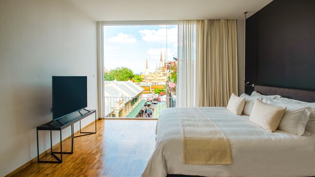 A hotel room with a large bed, a TV on a stand, and a view of a temple through the window. - Sala Rattanakosin Bangkok (Bangkok)