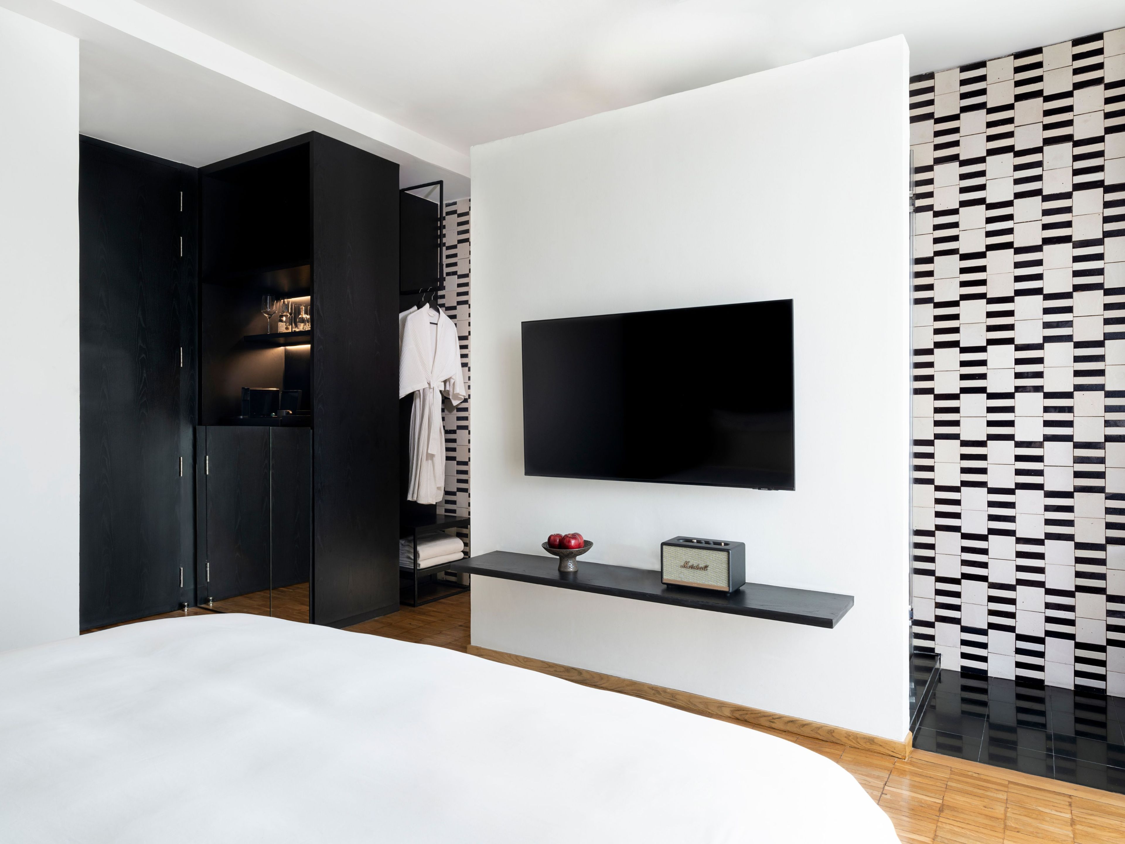 Una moderna camera d'hotel con TV a schermo piatto fissata al muro, un comodino con radio, un armadio e una parete decorata con un motivo.