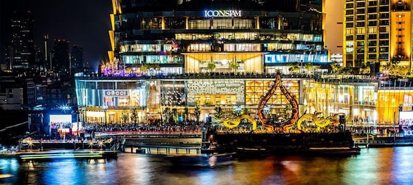 A waterfront hotel with multiple floors, luxury brand stores, and a prominent illuminated dragon sculpture. - Sala Rattanakosin Bangkok (Bangkok)