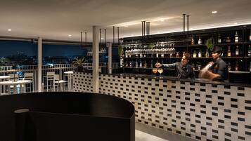 A bar area with a checkered wall pattern, a bar counter, and a city view at night.