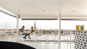 A balcony with white railings and wicker furniture, overlooking a cityscape with a prominent tower. - Sala Rattanakosin Bangkok (Bangkok)