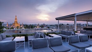 Una terraza en la azotea con mobiliario exterior, vista de un río y un templo al fondo.