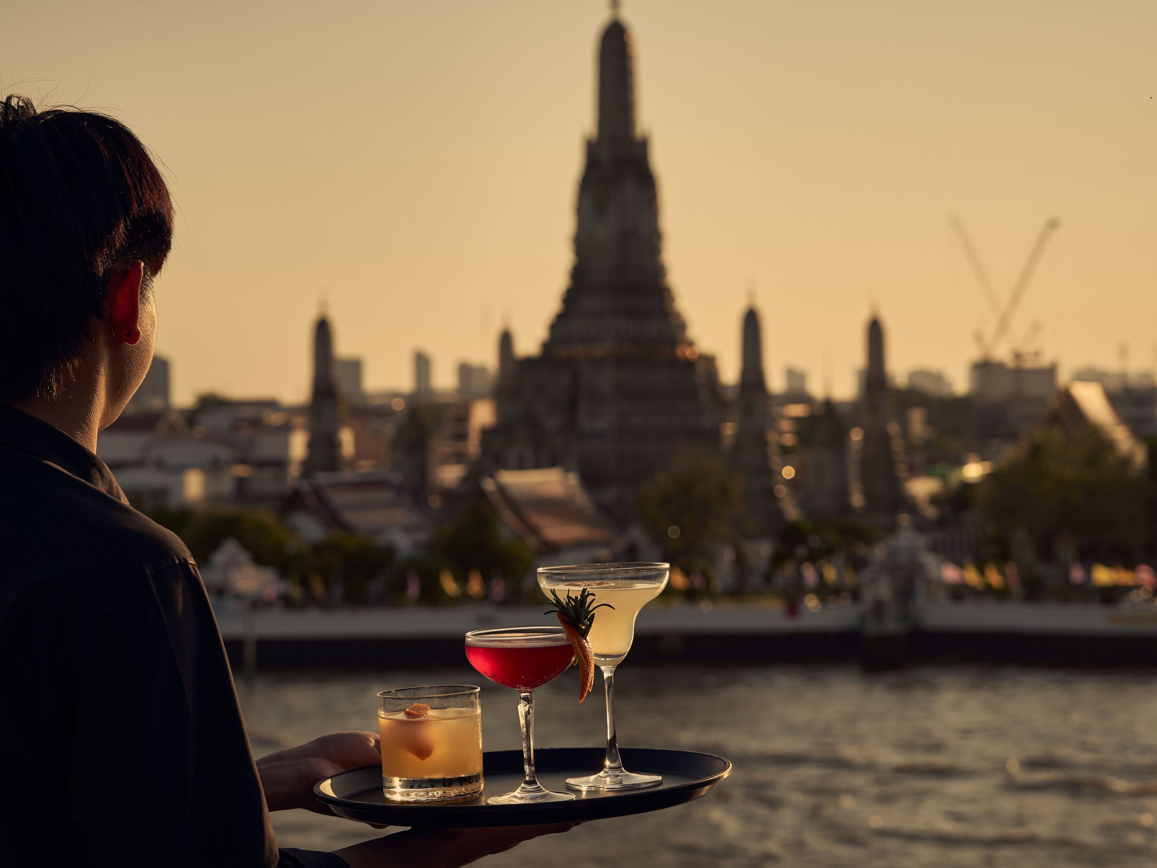 A person holding a tray with two drinks and a cityscape in the background.