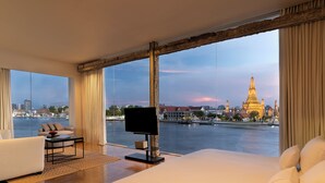 Habitación de hotel con una cama grande, televisión, sofá y vistas a un río y un templo.