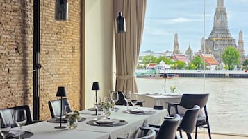 A dining area with a view of a river and a temple in the background.