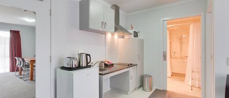 A compact kitchen with white cabinets, a countertop, and a built-in stove. There is a trash can and a microwave on the counter.