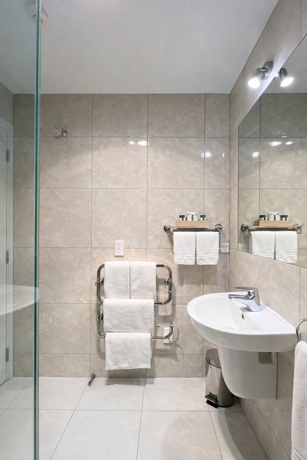 A modern bathroom with a glass shower enclosure, a white sink, and a vanity with a mirror.