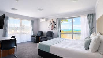 A hotel room with a large bed, two armchairs, a desk, and a TV.