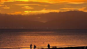 Ein Sonnenuntergang über dem Wasser, silhouettenhaft abgebildete Personen am Ufer.
