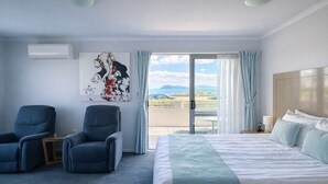 Ein Hotelzimmer mit einem Bett, zwei Sesseln, einem Gemälde und Blick ins Freie.