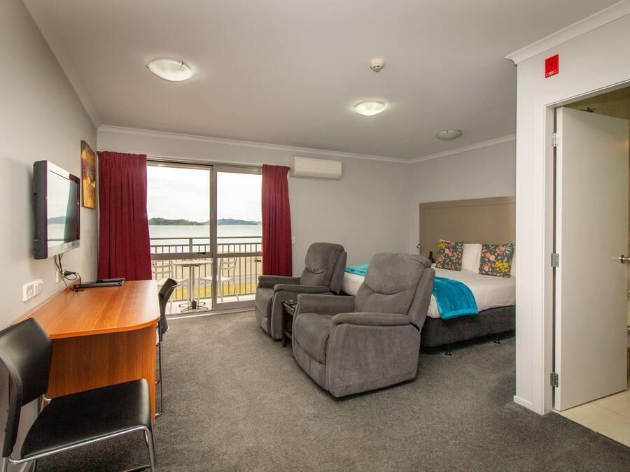 A hotel room with a balcony, a desk with a chair, a sofa, and a bed.